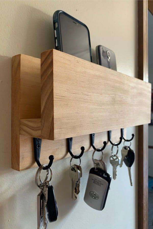A shelf with mobile phones on it and several small hooks below for keys